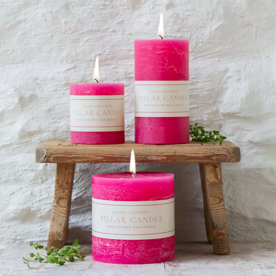 Bright pink pillar candles in 3 sizes on a small wooden bench with foliage