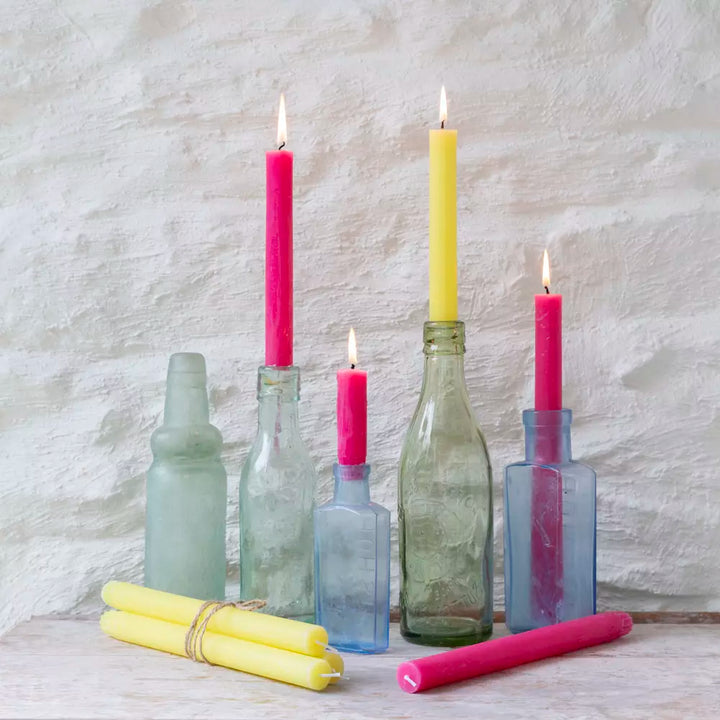 Bright pink and pastel yellow dinner candles lit in bottles 