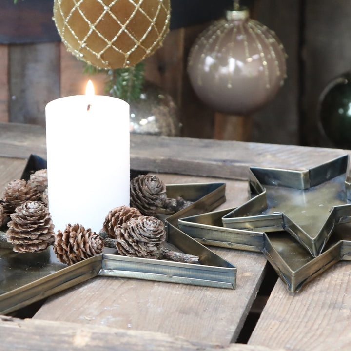 three antique brass star shaped trays with candle and pine cones baubles in background