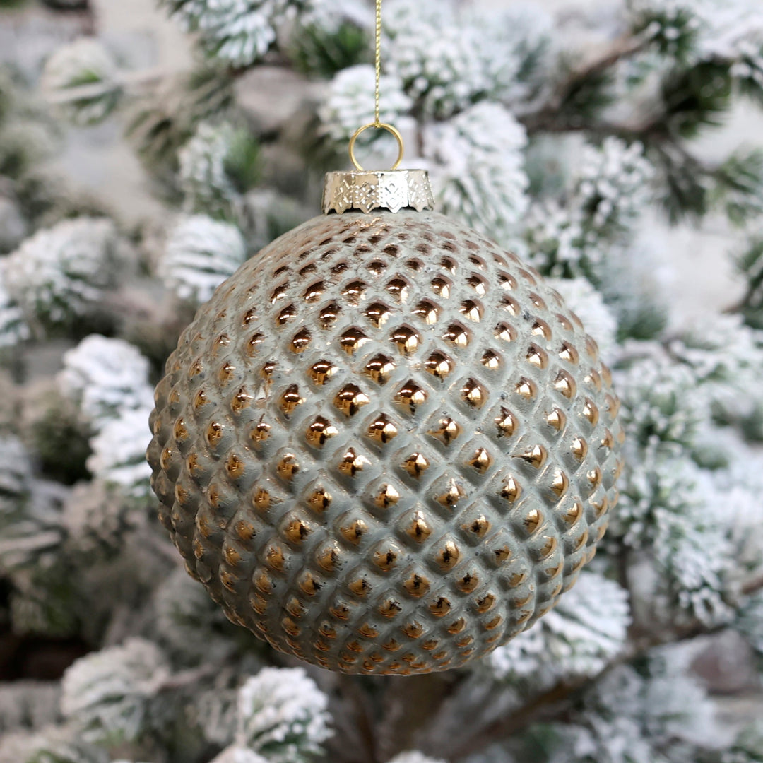 green and gold large Christmas bauble in front of snowy fir tree