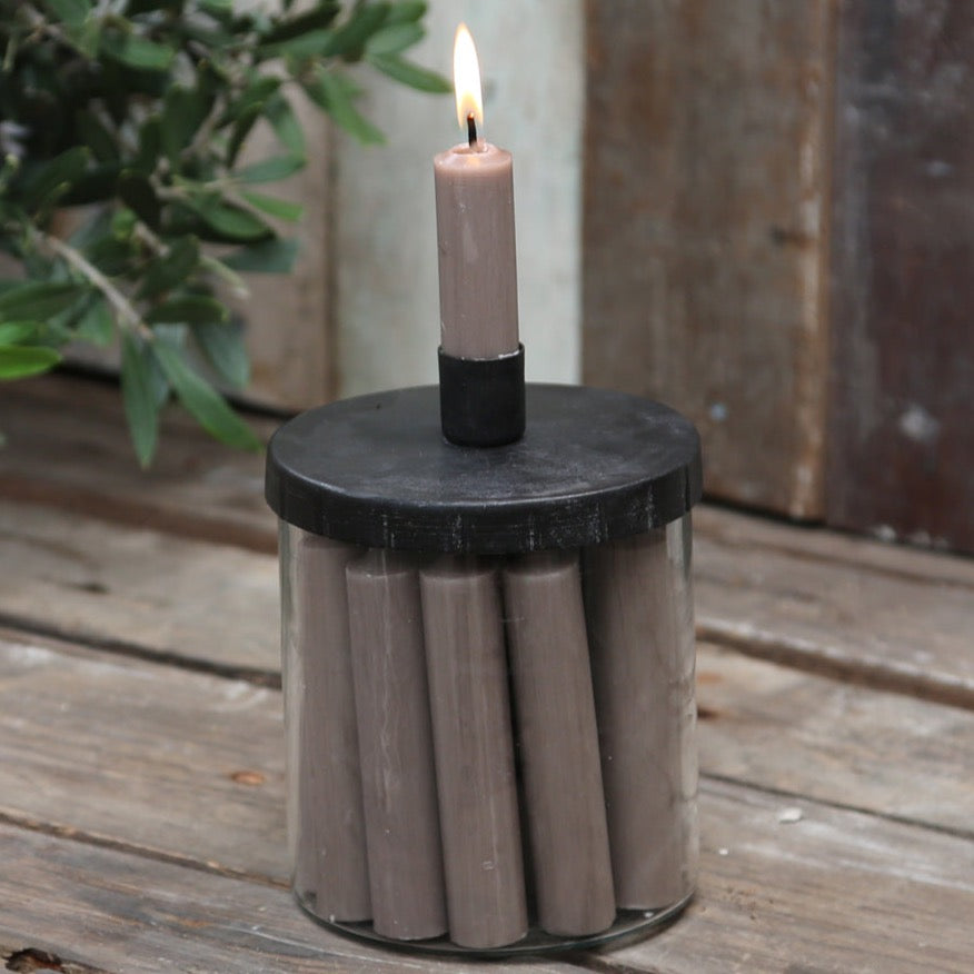 Scandi style candle jar with holder. Candle lit and jar on a wooden table with foliage in backgroud