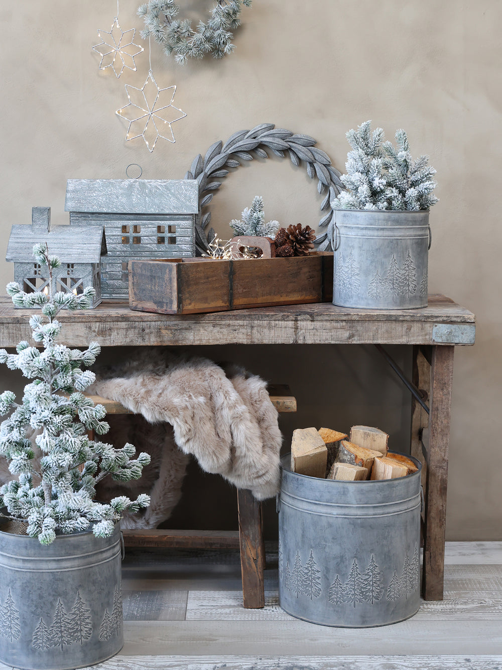 Fir tree zinc buckets filled with Christmas trees and logs with wooden table and bench with fur throw and metal house decorations