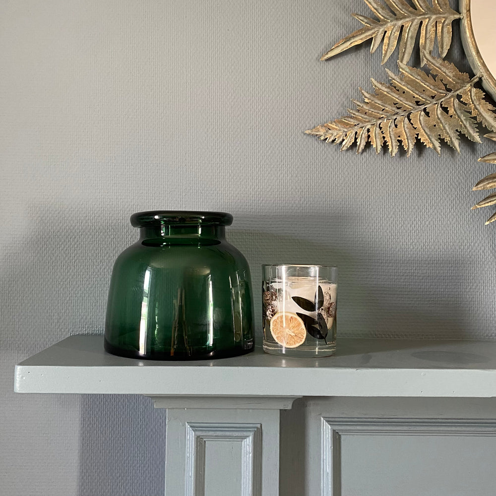 Green glass vase on mantel with candle against blue wall